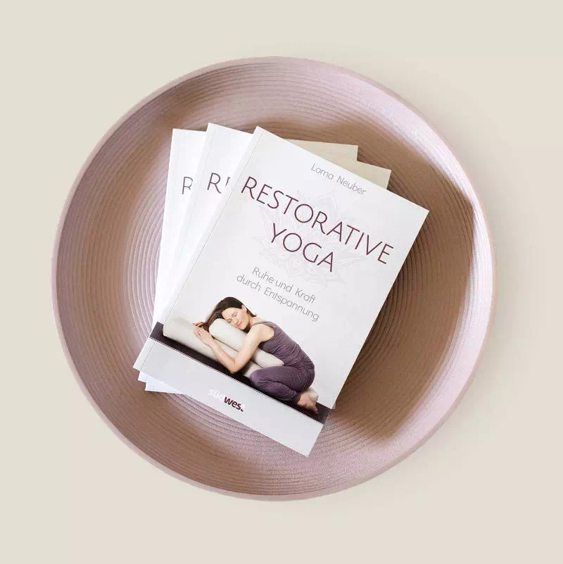 3 Bücher liegen in einer Schale mit dem Titel Restorative Yoga. Ruhe und Kraft druch Entspannung
